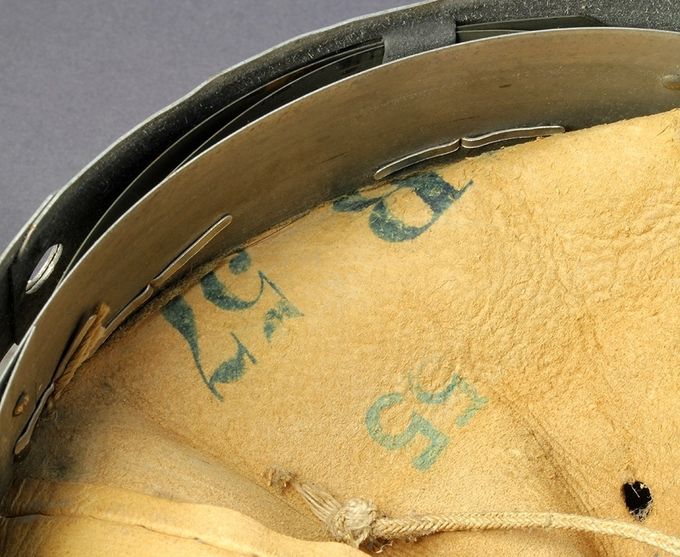 Markings on the inside of the leather. The number 57 indicates the size in cm of the inner metal band and the number 55 is the size for the wearer’s head, which is also is marked with an ink stamp on one of the tongues. The liner has the size of 62 and the size of the outer metal band is measured to be approximately 61 cm. Notice the lacking wool strip which has been cut off and the split aluminum rivets which secure the leather to the metal band.