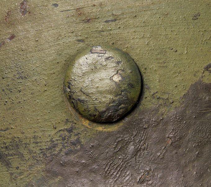 Close-up picture of a rivet head and the green and brown paint.