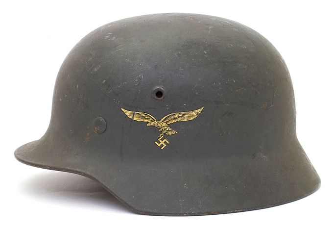 The M40 was produced from 1940 until mid-1942 (with the exception of the Quist factory) and as can be seen, the air vents are pressed into the sides of the shell during the manufacturing process. The helmet shown is a Q64 and has a an eagle spreading its wings in flight and clutching a swastika. This helmet is a Luftwaffe helmet (the German Air Force) and as was typical of M40 helmets, has insignia on the left side only. A Wehrmacht directive in March 1940 mandated that the national shield on the right side of the helmet be removed. From that point on, German helmets featured insignia on the left side only, with Police Troops being the exception. The smooth shiny paint was replaced by dull, textured paint. The crown is slightly more rounded in shape compared to the M35. The helmet shown has Luftwaffe mid-blue textured paint. From late 1940 the zinc-coated brass rivets were replaced by zinc-coated steel rivets which provided more strength.
 